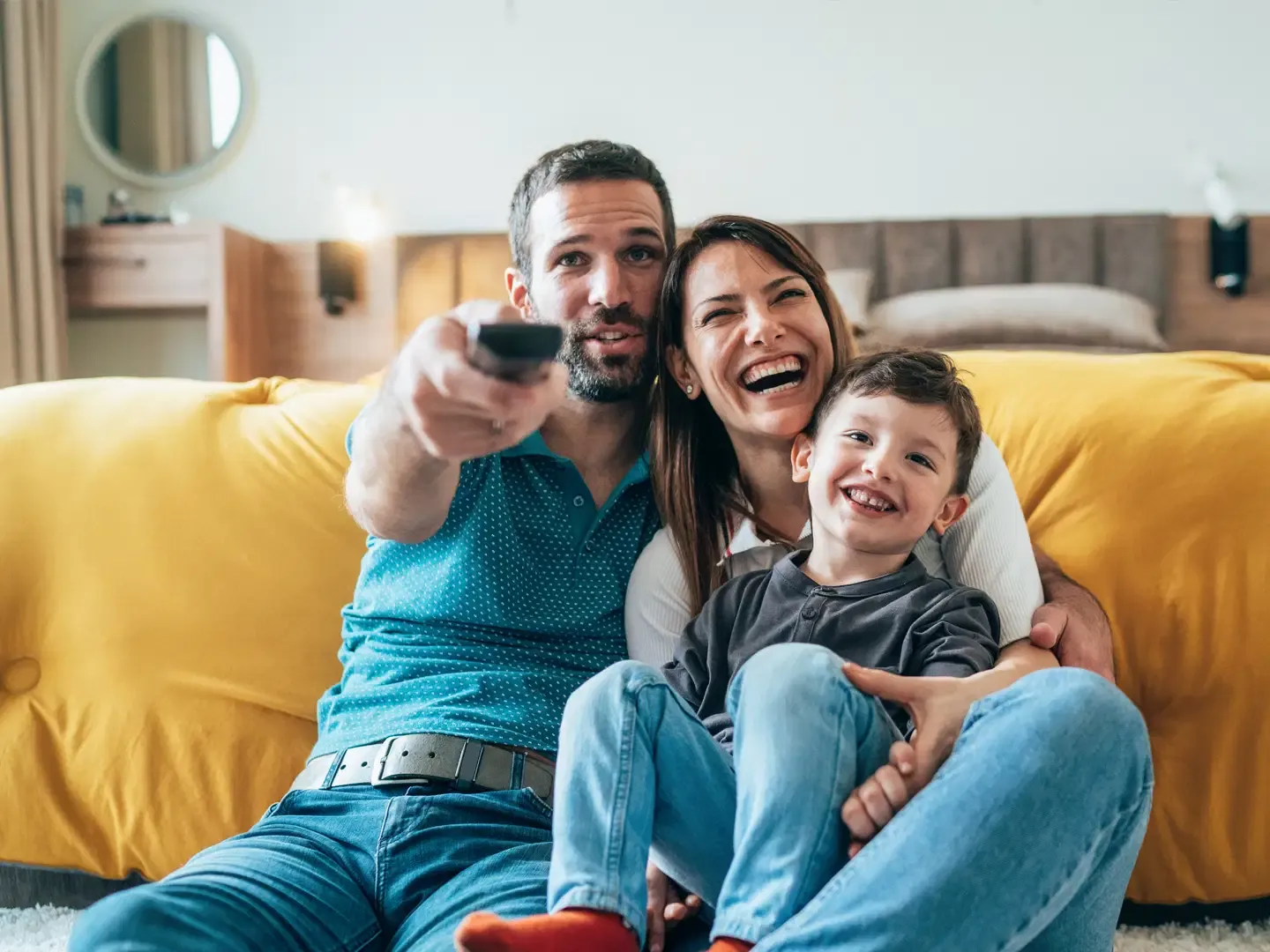 A happy family with a young boy sitting together on the floor and laughing while watching television.
